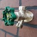 A wall-mounted non-freeze anti-siphon hydrant with a green handle attached to a brick wall.