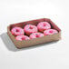 A cardboard box containing several pink iced donut rings with colorful sprinkles.