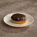 A Boston creme donut with chocolate icing on a white plate.