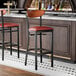A black metal bar stool with a burgundy vinyl seat and an antique walnut wood backrest.