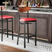 A black bar stool with a red vinyl seat and an antique walnut wood back, shown at a bar counter.