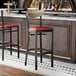 A black metal bar stool with a burgundy vinyl seat and a driftwood-finished wooden backrest.
