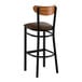 A bar stool with a black metal frame, dark brown vinyl seat, and a curved vintage wood backrest.