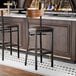 A black finish bar stool with a dark brown vinyl seat and a vintage wood back.