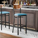 A black finish bar stool with a blue vinyl seat and a vintage wood back, shown unassembled at a bar counter.