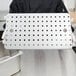 A person holding a Vollrath stainless steel tray with holes in it.