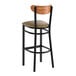 A black metal bar stool with a taupe vinyl seat and a curved vintage wood backrest.