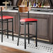 A black bar stool with a red vinyl seat and a curved wooden backrest.