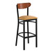 A black metal bar stool with a light brown vinyl seat and an antique walnut wood backrest.