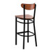 A bar stool with a black metal frame and an antique walnut wood seat and backrest.