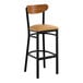 A black metal bar stool with a light brown vinyl seat and a curved wooden backrest.
