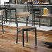 A black metal chair with a driftwood-finished wooden seat and backrest, shown in a bar or restaurant setting.