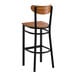 A bar stool with a black metal frame and a vintage wood seat and backrest.