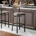 A black metal bar stool with a taupe vinyl seat and a driftwood-finished wooden backrest.