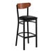 A black metal bar stool with a black vinyl seat and an antique walnut wood backrest.