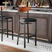 A black metal bar stool with a black vinyl seat and an antique walnut wood backrest.