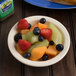 A Carlisle tan melamine grapefruit bowl filled with fruit on a table.