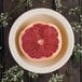 A half of a grapefruit in a Carlisle tan melamine bowl surrounded by small flowers.