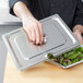 A hand using a Vollrath stainless steel slotted lid to open a metal tray with salad in it.