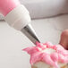 A metal leaf piping tip attached to a piping bag is being used to decorate a cupcake with pink icing.