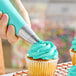 An open star piping tip being used to decorate a cupcake with blue frosting.