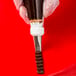 A metal basketweave piping tip attached to a piping bag being used to pipe chocolate icing.