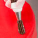 A closed star piping tip being used to pipe chocolate frosting onto a red cake surface.