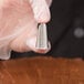A stainless steel leaf piping tip held by a gloved hand.