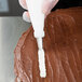 A piping bag fitted with a metal leaf piping tip is being used to decorate a chocolate-frosted cake.