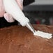 A metal leaf piping tip being used to decorate a chocolate-frosted cake with white icing.
