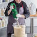 A green heavy-duty immersion blender being used to mix a large container of batter or liquid.