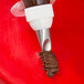 A metal curved petal piping tip attached to a piping bag, dispensing chocolate frosting onto a red surface.