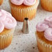 An open star piping tip made of metal, surrounded by cupcakes with pink frosting.