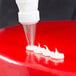 An open star piping tip being used to pipe white icing onto a red cake surface.