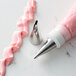 A metal ruffle piping tip and a piping bag filled with pink icing, used for cake decorating.