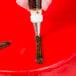 An open star piping tip being used to pipe chocolate frosting onto a red surface.