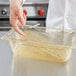 A hand placing a Vollrath amber high heat drain tray into a clear container.