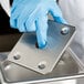 A person wearing blue gloves using a Vollrath stainless steel false bottom drain tray.