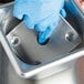 A person wearing blue gloves using a Vollrath stainless steel false bottom in a metal container.