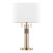 A gold table lamp with a cylindrical base and a white linen drum shade.