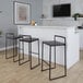 A set of black metal stackable low-back barstools with espresso bamboo seats placed at a white bar counter.