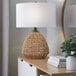 A table lamp with a natural rattan base and a white linen drum shade.