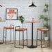 A set of two black metal barstools with low backs and camel-colored faux leather seats.