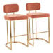 A pair of barstools with gold metal frames and salmon-colored fabric seats and backs.