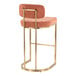 A modern barstool with a gold metal frame and salmon-colored fabric seat and backrest.