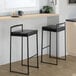 A pair of black metal stackable low-back barstools with black faux leather seats.