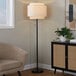 A black floor lamp with a beige linen tiered shade.