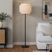 A black floor lamp with a beige linen tiered shade.