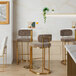 A pair of gold metal barstools with brown fabric backs and seats placed at a high table in a modern setting.