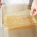 A hand using a Vollrath Super Pan drain tray to put food in a plastic container on a counter.